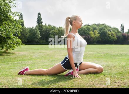 Jeune blonde blanche femme dans sa fin 20s - 30s portant des vêtements d'athlétisme pour faire des exercices d'étirement. Banque D'Images