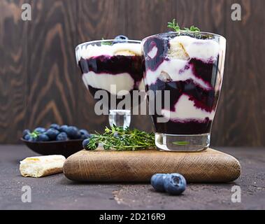 Dessert au mascarpone ou à la ricotta, bleuets et biscuit en verre sur fond de béton foncé. Pas de cheesecake ni de tiramisu cuit au four. Banque D'Images