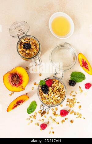 Granola ou muesli faits maison sur fond de pierre. Ingrédients pour un petit déjeuner sain - granola, baies, pêche, menthe et miel. Vue de dessus. Banque D'Images