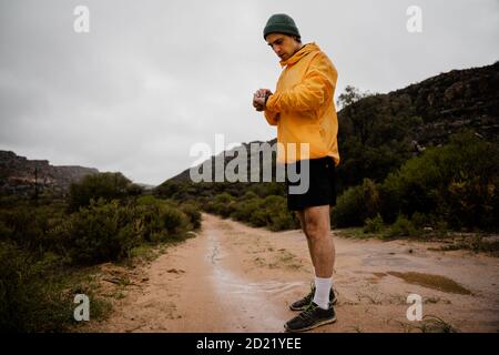 Jeune athlète masculin actif défilant sur une montre intelligente sur un sentier de randonnée en montagne. Banque D'Images