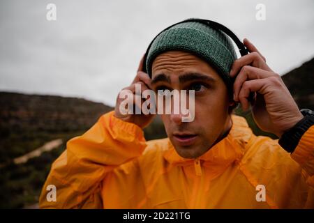 Une coupe attrayante pour les jeunes athlètes masculins qui se concentrent sur l'écoute de musique dans un casque tout en courant sur un sentier de montagne humide avec une montre intelligente Banque D'Images