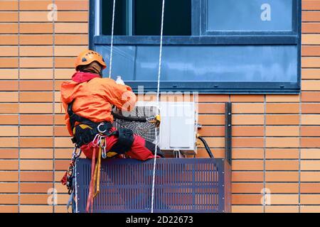 Un travailleur installe un climatiseur sur le mur de un bâtiment résidentiel Banque D'Images