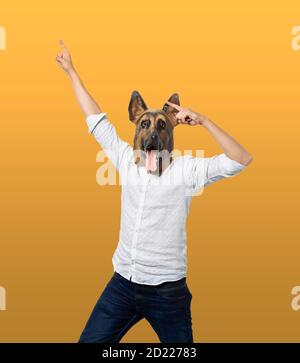 Homme portant un masque de chien regardant l'appareil photo et pointant vers le haut dans la célébration. Arrière-plan jaune isolé. Prise de vue moyenne. Banque D'Images