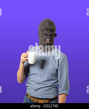 Homme portant un masque de gorille tenant une tasse de café sur fond bleu isolé. Prise de vue moyenne. Banque D'Images