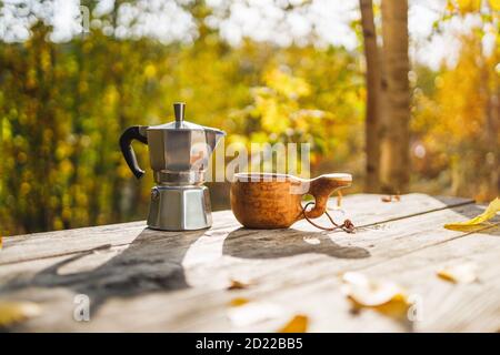 Cafetière et tasse en bois kuksa sur une table en bois dans la forêt d'automne. Tôt le matin. Lever du soleil. L'arrière-plan est flou. Banque D'Images