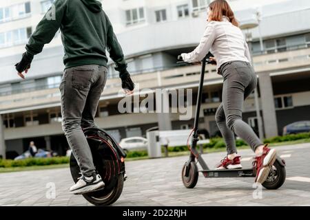 Jeune homme à cheval sur un monocycle et jeune femme en tenue décontractée en voiture sur un scooter électrique dans la rue de la ville Banque D'Images