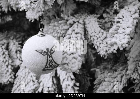 Boule vintage avec silhouette d'ange accrochée à l'arbre de Noël recouvert de neige. Carte de Noël vintage. Mise au point sélective. Photo vieillie. Noir et blanc. Banque D'Images