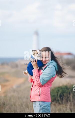 joyeux sourire belle jeune femme portant un survêtement tenant peu habillé chien de compagnie chihuahua pendant la randonnée en plein air Banque D'Images