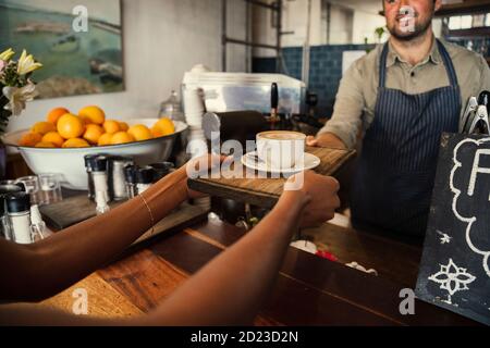 Un serveur souriant donne un latte chaud frais à une femme en funky café Banque D'Images