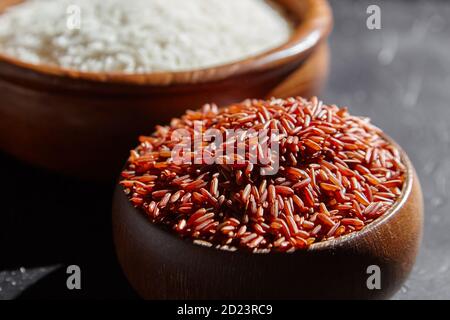 Riz rouge et blanc dans des bols en bois sur une table en pierre noire. Grains secs non cuits. Ingrédient pour cuisiner divers plats Banque D'Images