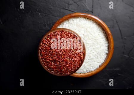 Riz rouge et blanc dans des bols en bois sur une table en pierre noire, vue de dessus. Grains secs non cuits. Ingrédient pour cuisiner divers plats Banque D'Images