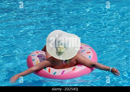 Femme en chapeau et bikini nageant sur anneau gonflable de donut dans la piscine. Vacances à la plage, détente et concept de loisirs Banque D'Images