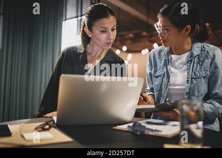 Deux jeunes femmes d'affaires diverses se sont concentrées sur leur travail pendant qu'elles étaient assises ensemble à une table dans un bureau moderne Banque D'Images