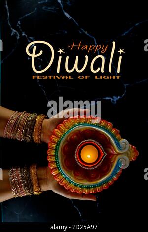 Happy Diwali - femmes mains avec henné tenant la bougie allumée isolé sur fond sombre. Clay Diya lampes allumées pendant Dipavali, festival hindou de lumières ce Banque D'Images