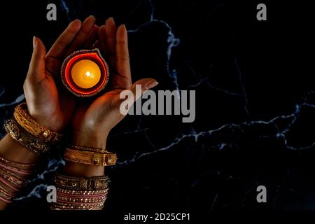 Happy Diwali - femmes mains avec henné tenant la bougie allumée isolé sur fond sombre. Clay Diya lampes allumées pendant Dipavali, festival hindou de lumières ce Banque D'Images