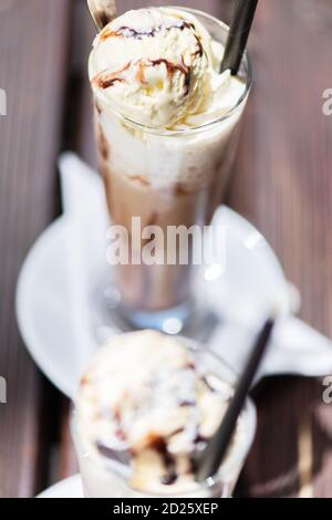 Café glacé sur une table en bois avec de la crème versée dans elle montrant la texture et l'aspect rafraîchissant de la boisson. Banque D'Images