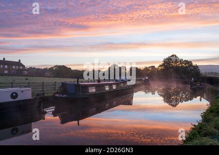 Un superbe lever de soleil au-dessus du canal de Leeds et Liverpool à Skipton, dans le parc national de Yorkshire Dales, tandis que les bateaux-canaux flottent sur le miroir de l'eau calme. Banque D'Images