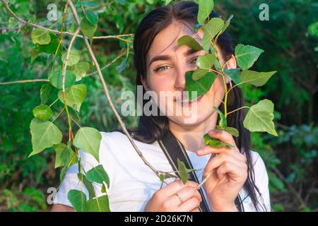 Portrait de femme avec des feuilles vertes d'une plante sur son visage. Superbe effet bokeh, mise au point sélective. La femme est heureuse et souriante. Concept nature, spa Banque D'Images