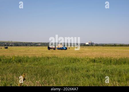 Région de Nizhny Novgorod, Russie - 8 juillet 2020 : camion bleu Kamaz avec une remorque transportant des rouleaux de foin à travers le champ fauchée, travaux agricoles dans le Banque D'Images