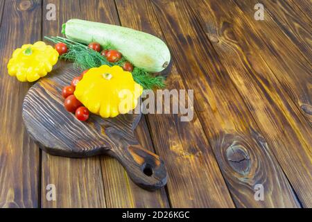 Légumes multicolores sur une table en bois sombre. Courgettes vertes, aneth, tomate cerise, mini moule à patty jaune écrasée différentes récoltes de légumes. Copie s Banque D'Images