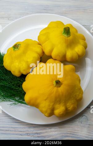 Trois courgettes rondes jaunes sur une plaque en gros plan. Mini patty de courge fraîche sur une table en bois, mise au point sélective. Banque D'Images