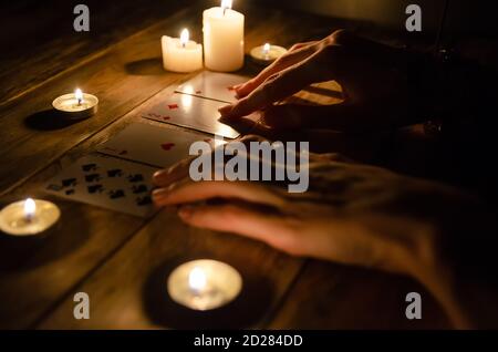 Mains d'un tueur de fortune et cartes sur la table, autour des bougies allumées dans le noir sur une table en bois. Concept de divination, magie Banque D'Images