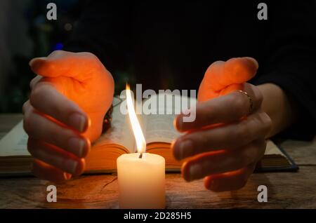 Mains près de la bougie et un livre sur la table. Concept de magie, éducation Banque D'Images