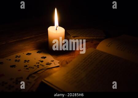 atmosphère mystique, cartes, un livre, une bougie allumée dans le noir sur une table en bois. Concept ésotérique, prédictions et récits de fortune Banque D'Images