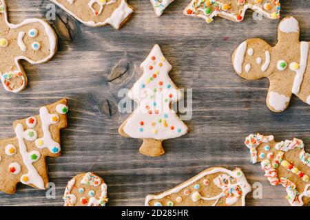 Gros plan des biscuits de pain d'épice de Noël sur une texture en bois. Sapins, petits hommes et cloches décorés de vernis blanc et de points multicolores. Banque D'Images