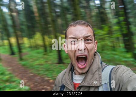 brunette homme criant dans la forêt d'une voix effrayée, portrait d'un homme hurlant avec sa bouche large ouverte dans la forêt d'automne Banque D'Images