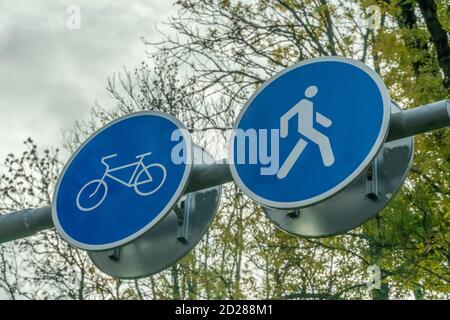 Deux panneaux routiers côte à côte pour piétons et cyclistes gros plan contre le ciel et les branches de l'arbre Banque D'Images