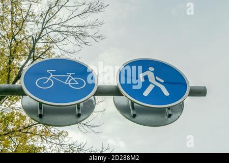 Deux panneaux routiers côte à côte pour piétons et cyclistes gros plan contre le ciel et les branches de l'arbre Banque D'Images