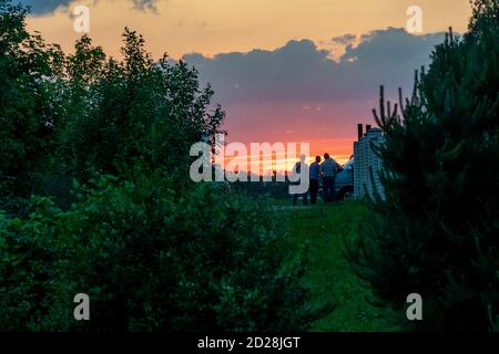 Au loin, trois hommes se tiennent près d'une voiture avec un capot ouvert et regardent à l'intérieur contre un magnifique coucher de soleil rose saumon. Banque D'Images