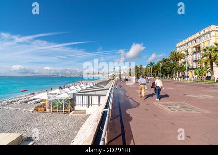 Les touristes apprécient une journée d'été ensoleillée le long de la Côte d'Azur en marchant sur la Promenade des Anglais et en profitant de la plage de galets le long de la baie des Anges. Banque D'Images