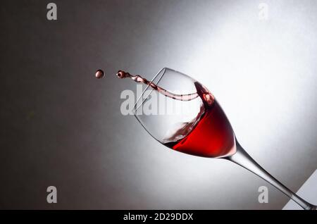 Verre aux éclaboussures, gouttes de vin rouge sur fond blanc. Gel des liquides en mouvement. Verre de vin rouge en angle avec espace de copie Banque D'Images