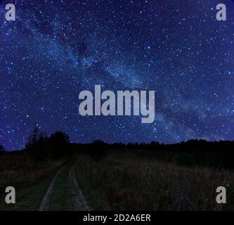 Magnifique paysage rural de nuit avec ciel étoilé et galaxie de la voie lactée. Des étoiles qui brillent sur la route sale à travers la prairie d'automne. Scintillant et léger Banque D'Images