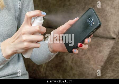 Les mains des femmes désinfectent un téléphone portable noir avec un aérosol antiseptique Banque D'Images