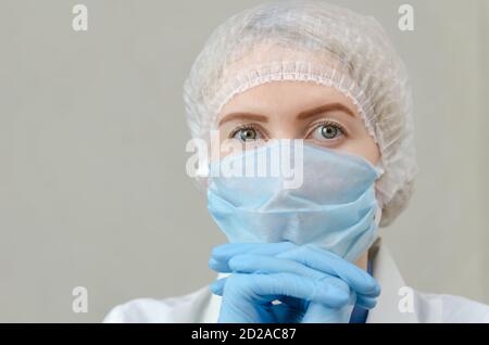 Portrait d'une belle jeune femme médecin dans une robe médicale, un masque médical et une casquette avec sa tête soutenue sur sa main. Médecin fatigué Banque D'Images