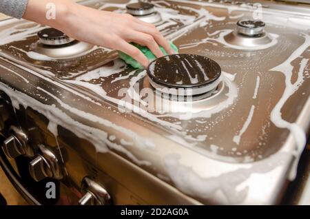 la main de femme lave un poêle à gaz gris en acier inoxydable avec une éponge en mousse verte. Nettoyage de la maison Banque D'Images