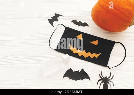 Halloween mal masque facial, citrouille, bouteille de gel de désinfection, chauve-souris et décorations d'araignée sur bois blanc. Célébrer Halloween 2020 de manière sécuritaire pendant co Banque D'Images