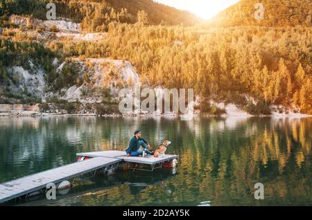 L'homme en tant que propriétaire de chien et son ami beagle chien sont assis sur la jetée en bois sur le lac de montagne et profiter du paysage pendant leur marche dans le th Banque D'Images