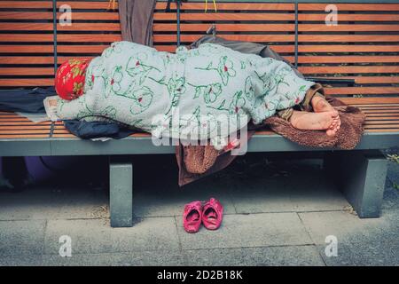 Grand-mère sans abri dans des vêtements propres et bien rangés dormant sur un banc. Granny errant dans la ville de ses chaussures et de poser sur vos affaires. Dans le parc de la ville Banque D'Images