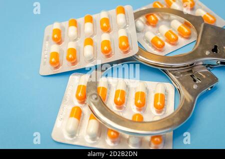 Menottes et beaucoup de pilules sur un fond bleu gros plan Banque D'Images