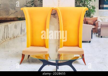 Grandes chaises jaunes à haut dossier dans le hall de l'hôtel. Mobilier avec table en verre dans l'intérieur en marbre de l'hôtel. Banque D'Images