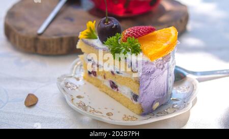 Gros plan gâteau de fruits d'anniversaire Slice dans assiette violet Delicious crème en couche Banque D'Images