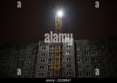 La grue de tour et les bâtiments de plusieurs étages inachevés sont construit la nuit sur un chantier de construction éclairé Banque D'Images