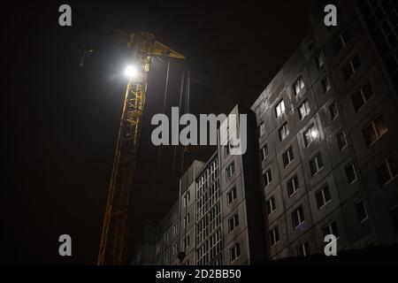 La grue de tour et les bâtiments de plusieurs étages inachevés sont construit la nuit sur un chantier de construction éclairé Banque D'Images