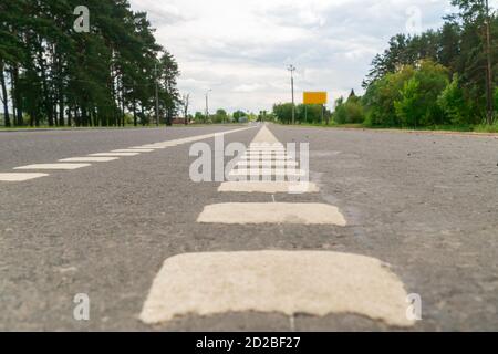 Lignes blanches brisées de marquages routiers, signalisation routière, arbres sur les bords de la route. Photo ci-dessous Banque D'Images