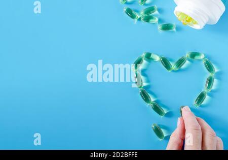 La main d'une femme présente le contour symbolique d'un cœur à partir de capsules à l'huile de poisson. Banque D'Images