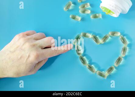 La main d'une femme présente le contour symbolique d'un cœur à partir de capsules à l'huile de poisson. Banque D'Images